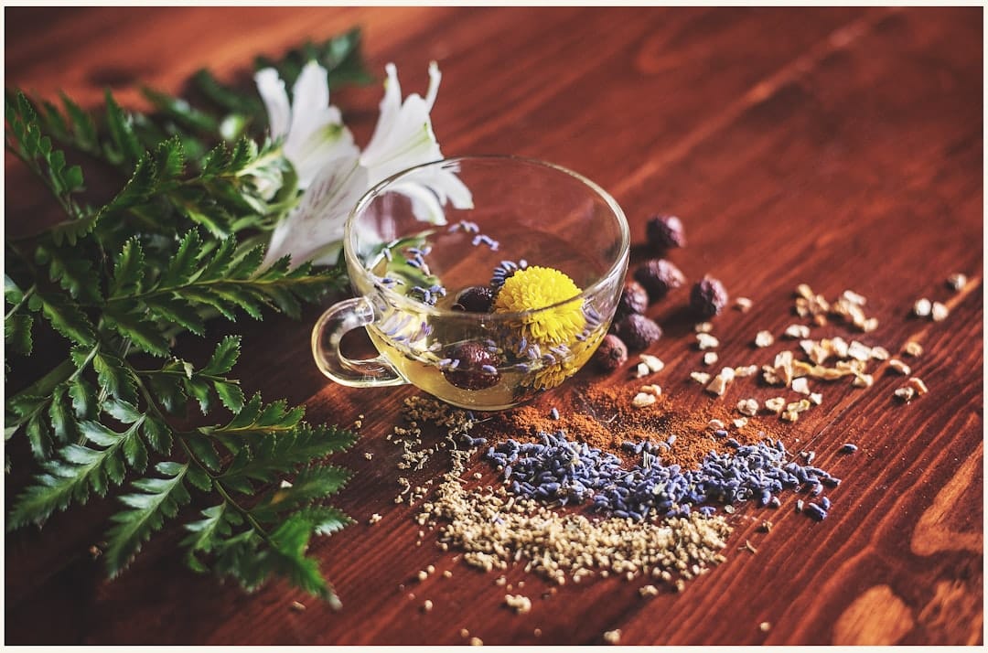 Steaming cup of pale herbal tea beside dried flower petals on a wooden table