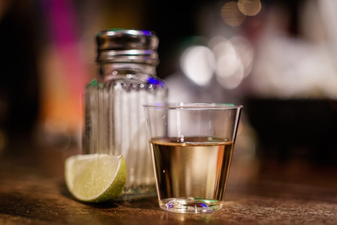 A small shot glass of clear tequila beside a lime wedge and a rim of salt