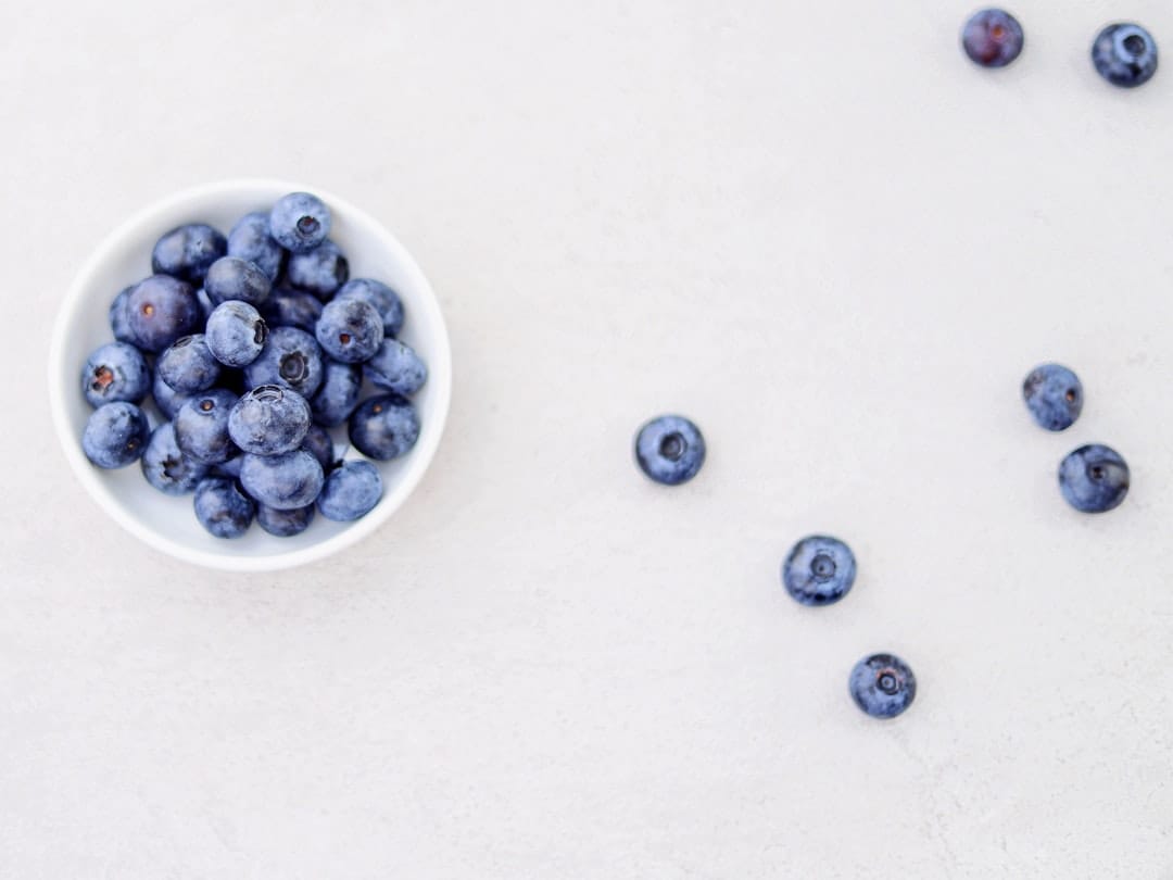 A white bowl heaped with plump fresh blueberries on a counter