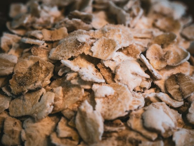 A heap of pale golden wheat germ flakes spilling from a wooden spoon