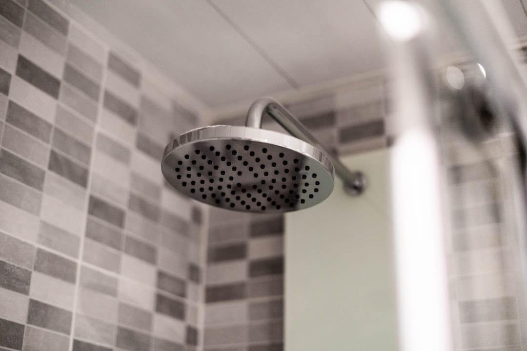 Warm water streaming from a chrome shower head against a tiled wall