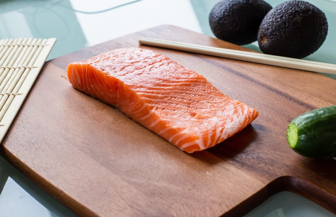 a sliced avocado beside a raw salmon fillet on wood