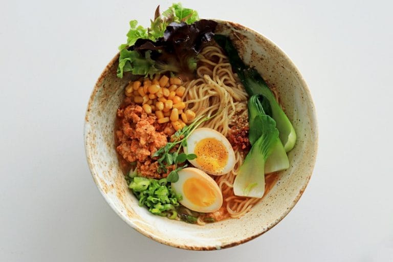 Steaming bowl of thin brown buckwheat noodles topped with sliced green onions