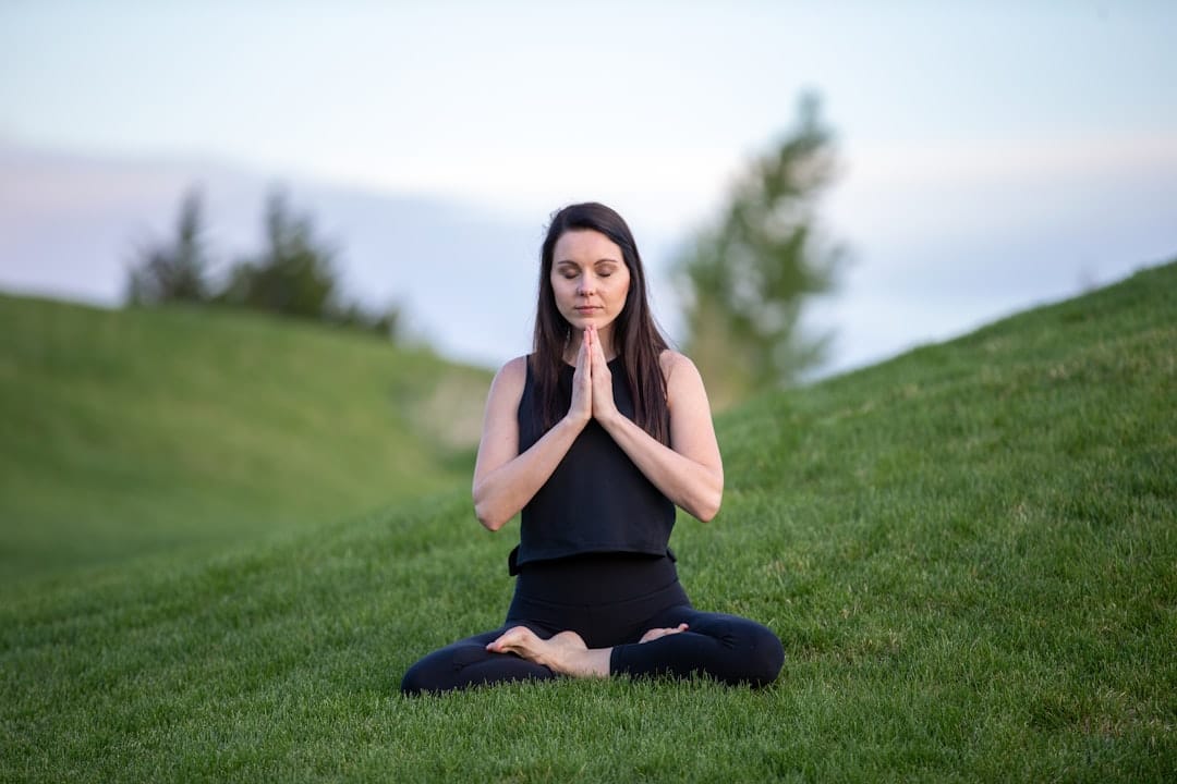 A woman sitting cross-legged meditating calmly in a green park
