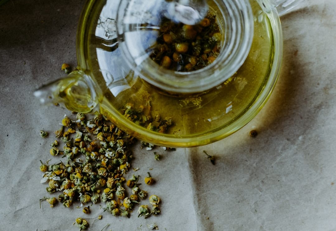 Pale golden chamomile tea in a clear glass cup with dried flowers nearby