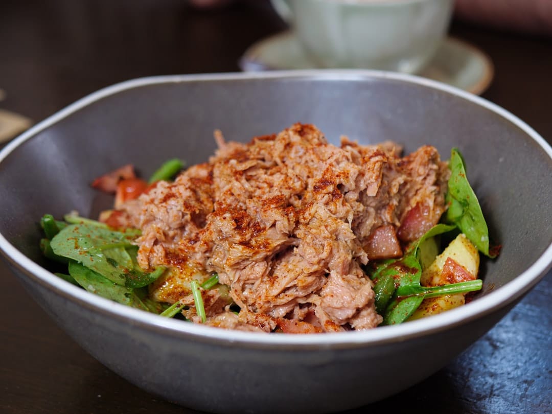 Tuna salad with greens, tomatoes, and corn in a white bowl