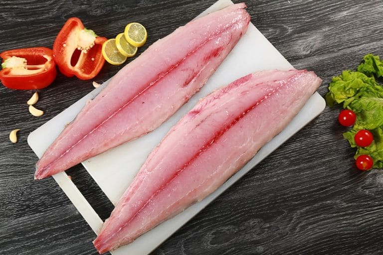 Raw white fish fillet on a wooden board with lemon wedges and parsley nearby