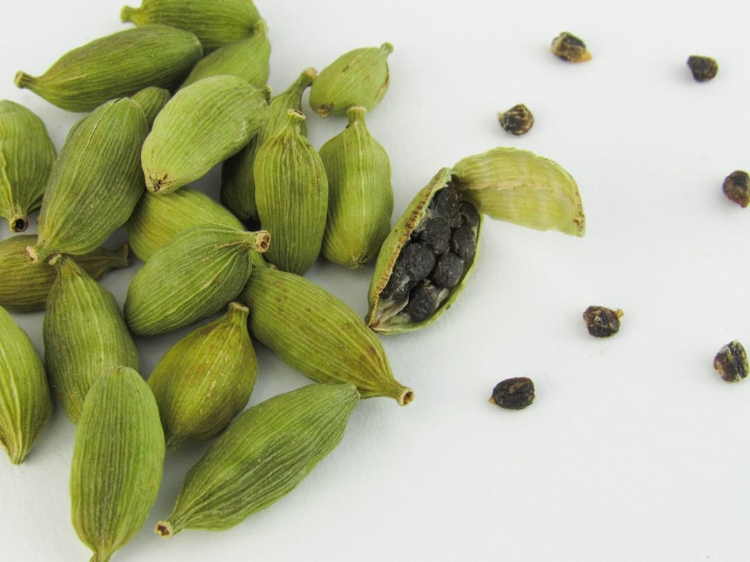 A pile of whole green cardamom pods on wood