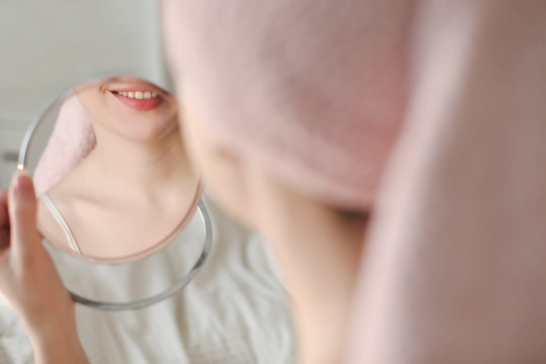 A person dabbing facial oil onto their cheek with a round cotton pad