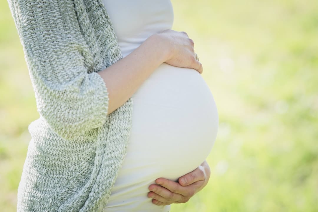 A smiling pregnant woman cradles her belly with both hands