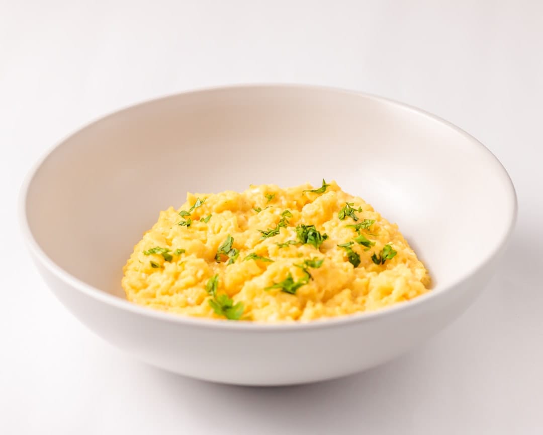 Fluffy soft scrambled eggs piled on a plate with a fork