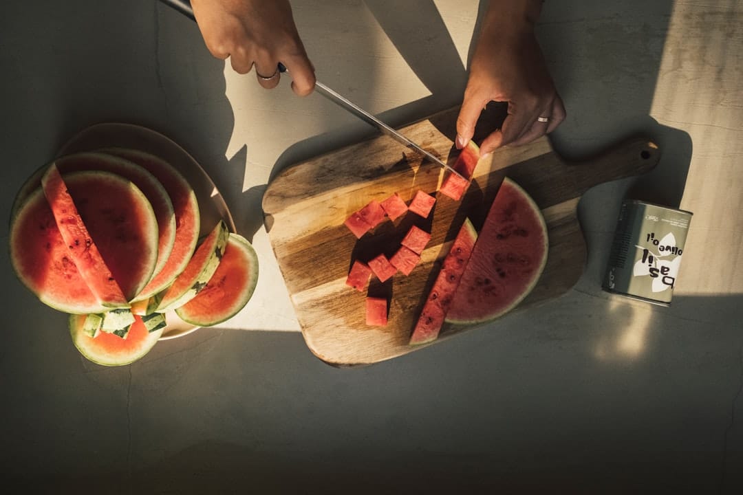 hands slicing a whole cantaloupe on a wooden cutting board