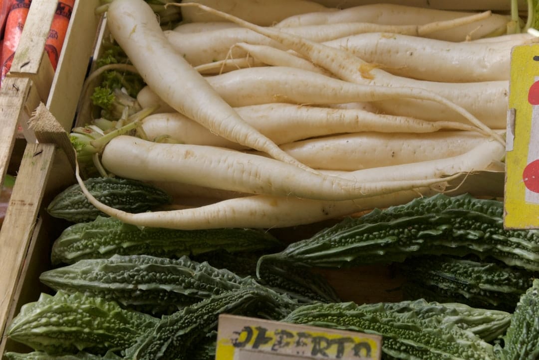 Unwashed root vegetables resting in a rustic wooden crate at a market