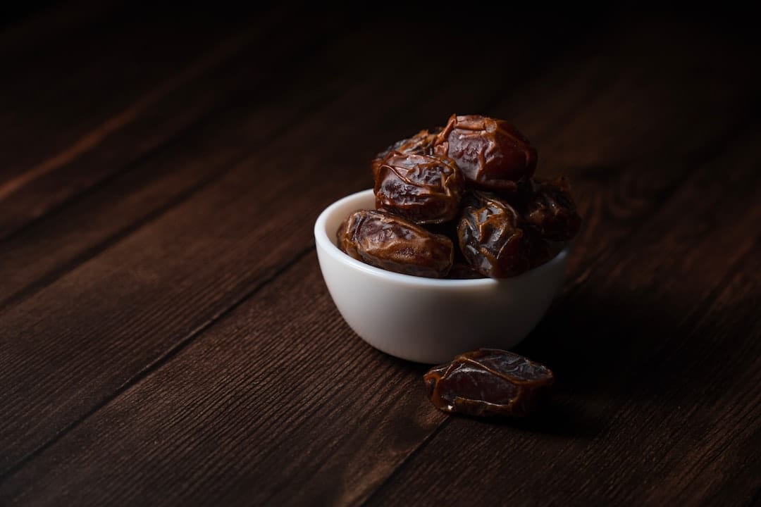 Whole dried dates piled in a rustic ceramic bowl on a wooden table