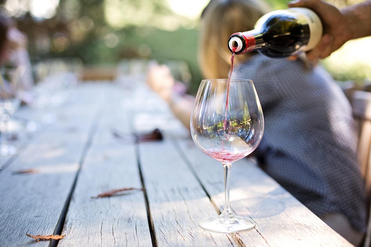 Red wine being poured into a glass pitcher of sliced fruit