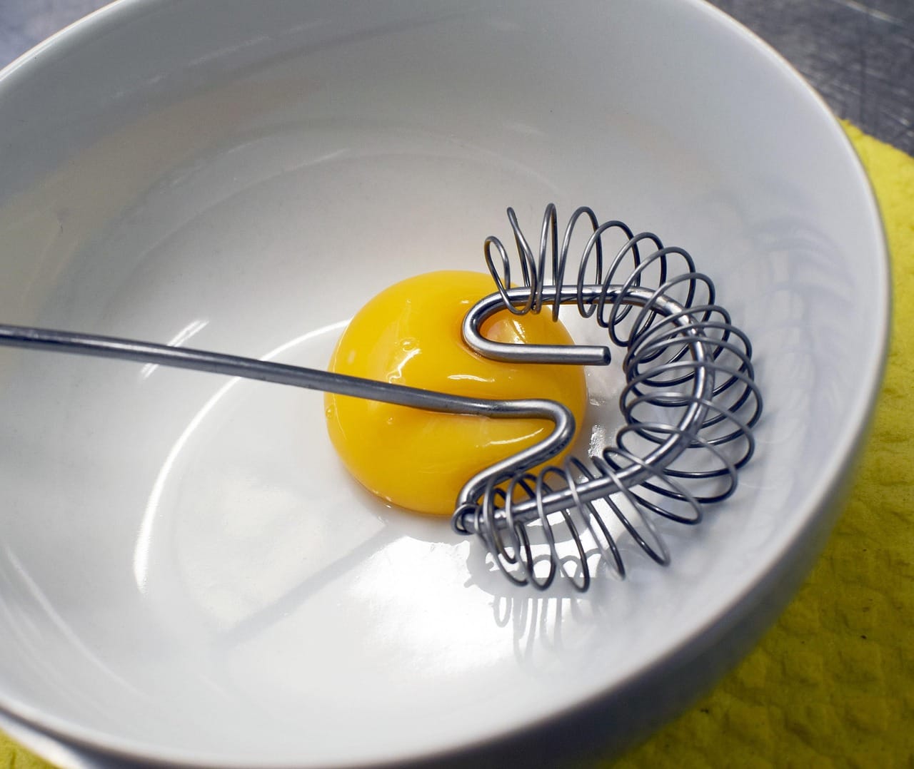 Egg yolks being whisked in a glass bowl with a balloon whisk