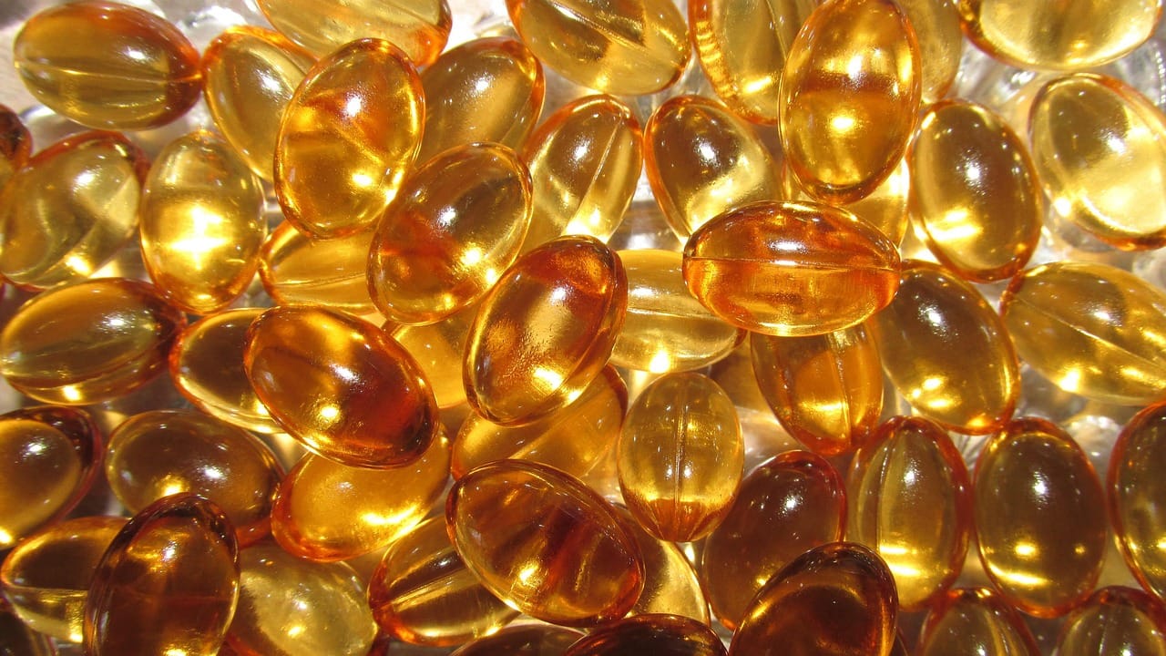 Golden vitamin E softgel capsules scattered on a white surface with one pierced open