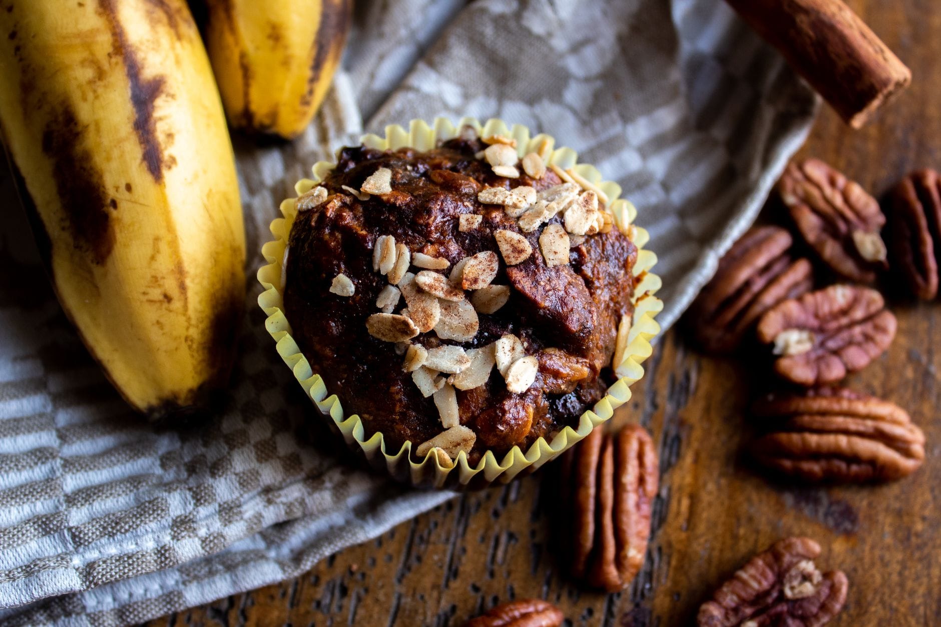 A tray of golden banana muffins cooling on a wooden board beside ripe bananas