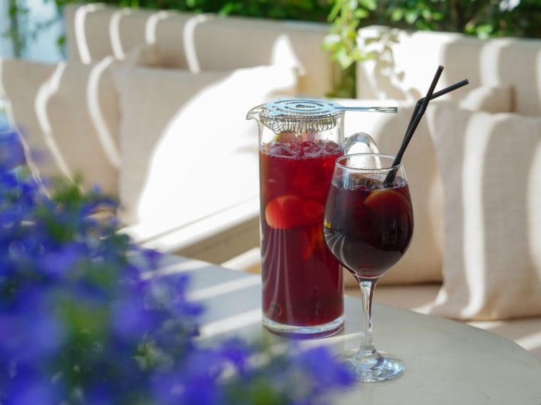 A glass pitcher of deep red sangria with orange slices and ice
