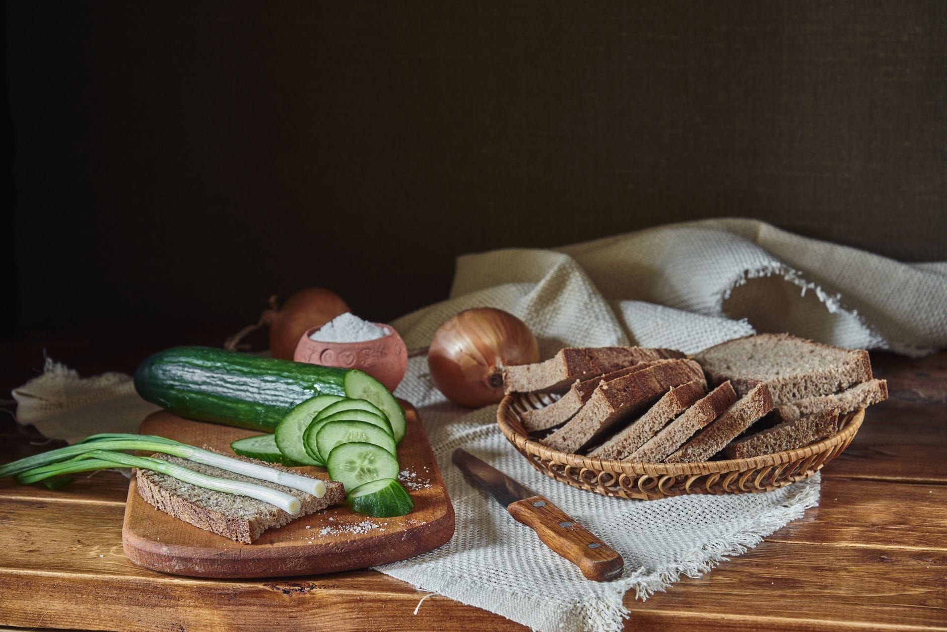 Sliced whole grain bread, leafy greens, and fresh vegetables on a board