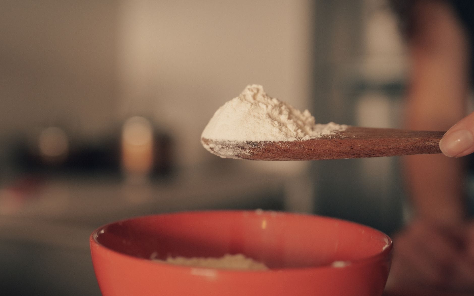 A small white bowl of baking soda beside a metal spoon
