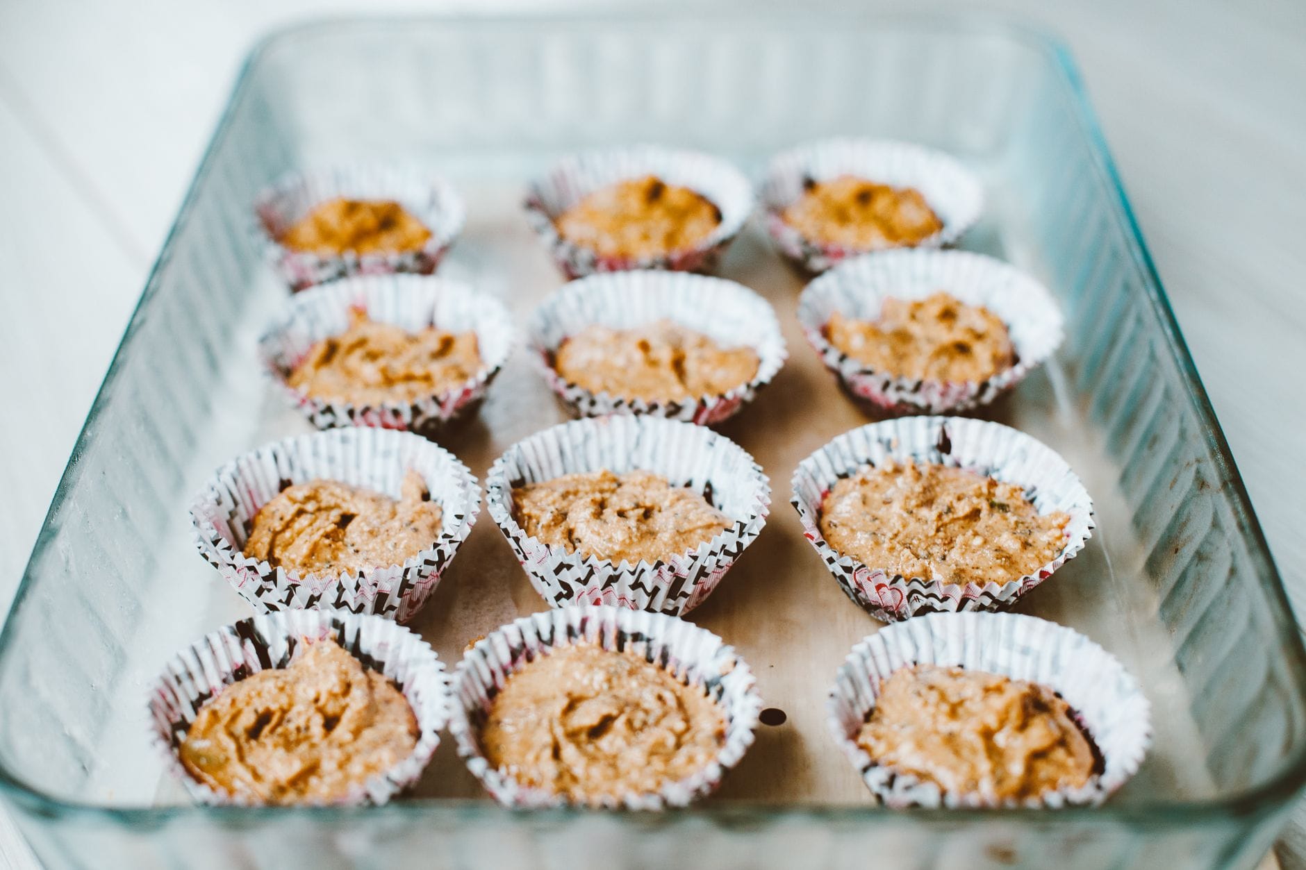 Muffin batter being spooned into a lined metal muffin tin
