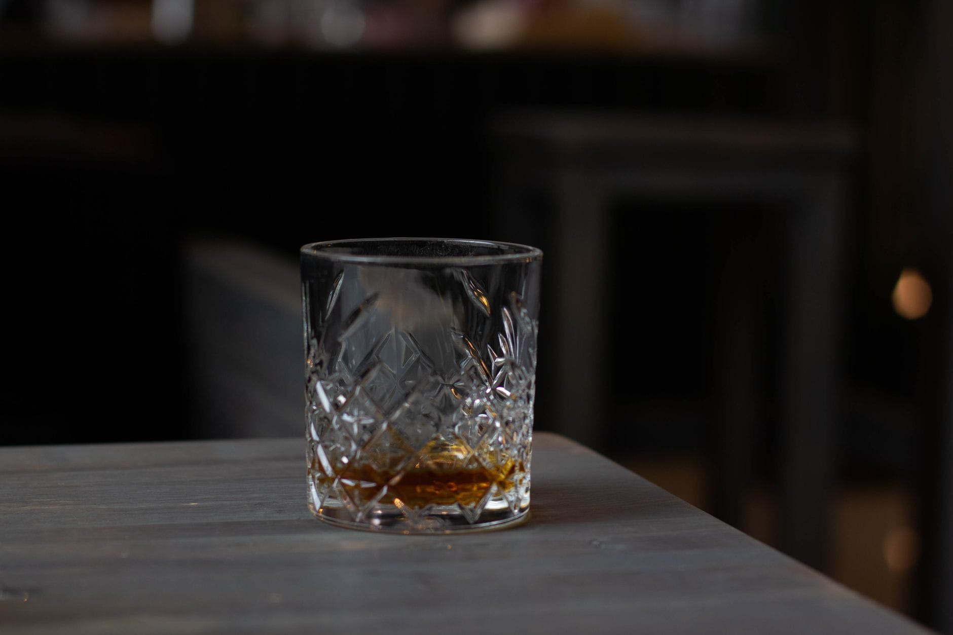 A bottle of amber spirit beside a short glass on a dark bar top