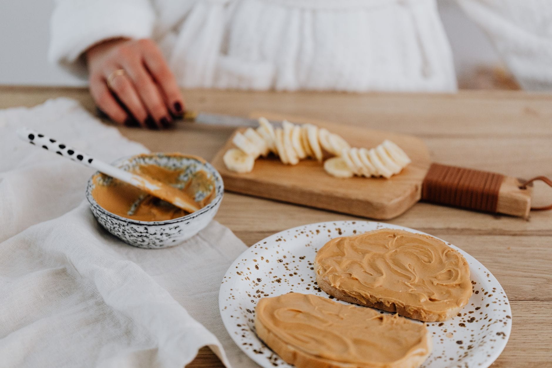 Ripe spotted bananas beside an open jar of peanut butter on a counter