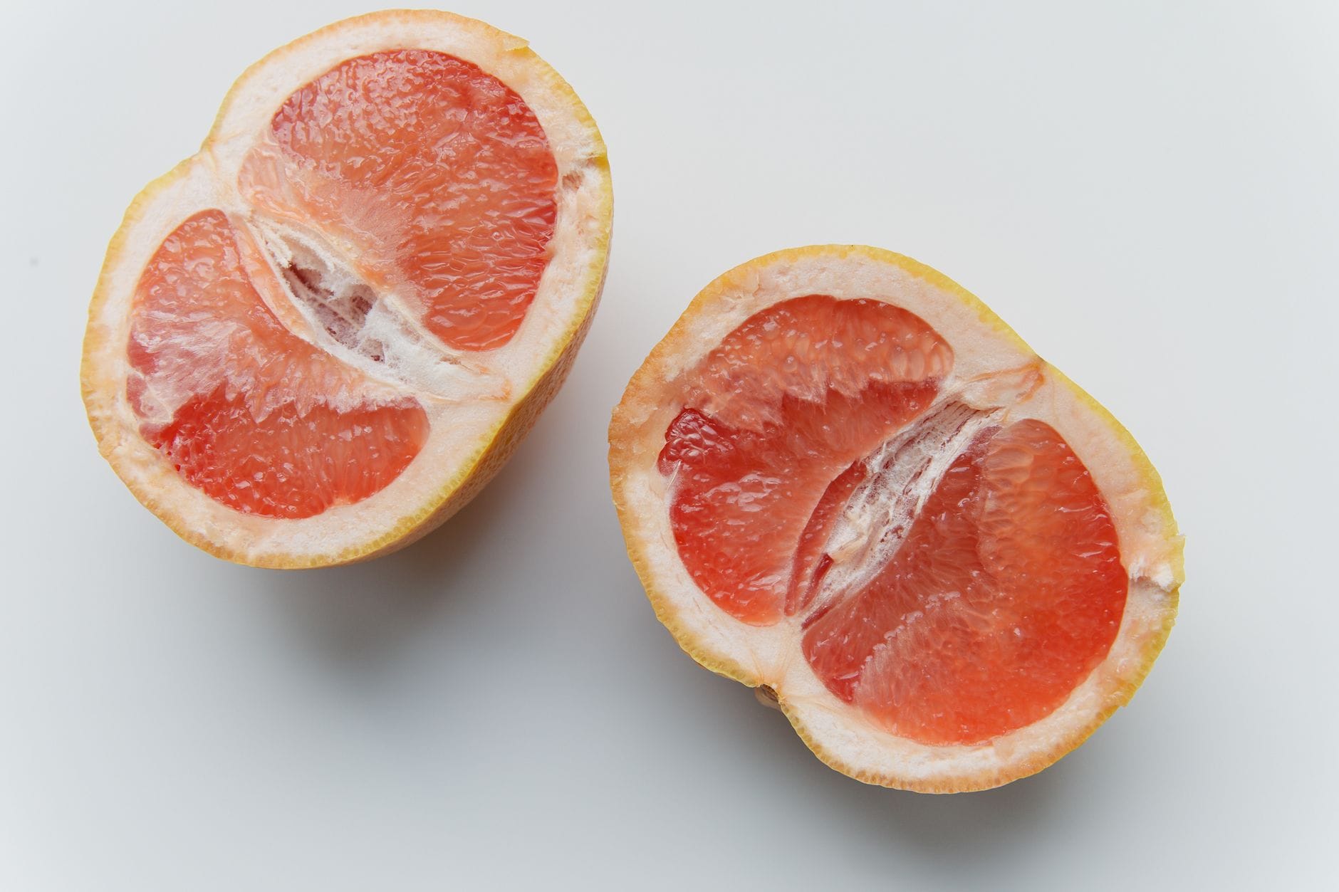 Two ruby grapefruit halves cut side up on a marble counter