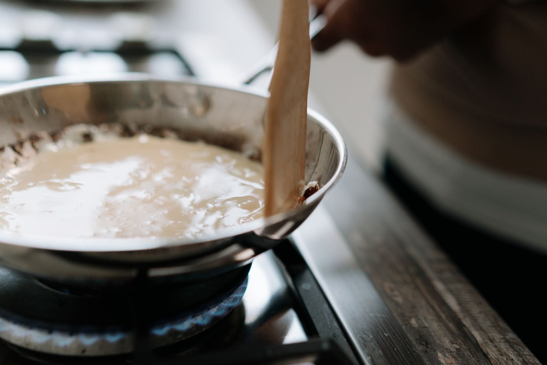 A wooden spoon stirring pale custard in a stainless steel saucepan
