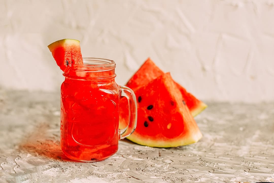 A tall glass of pink watermelon juice with a straw and mint on a table