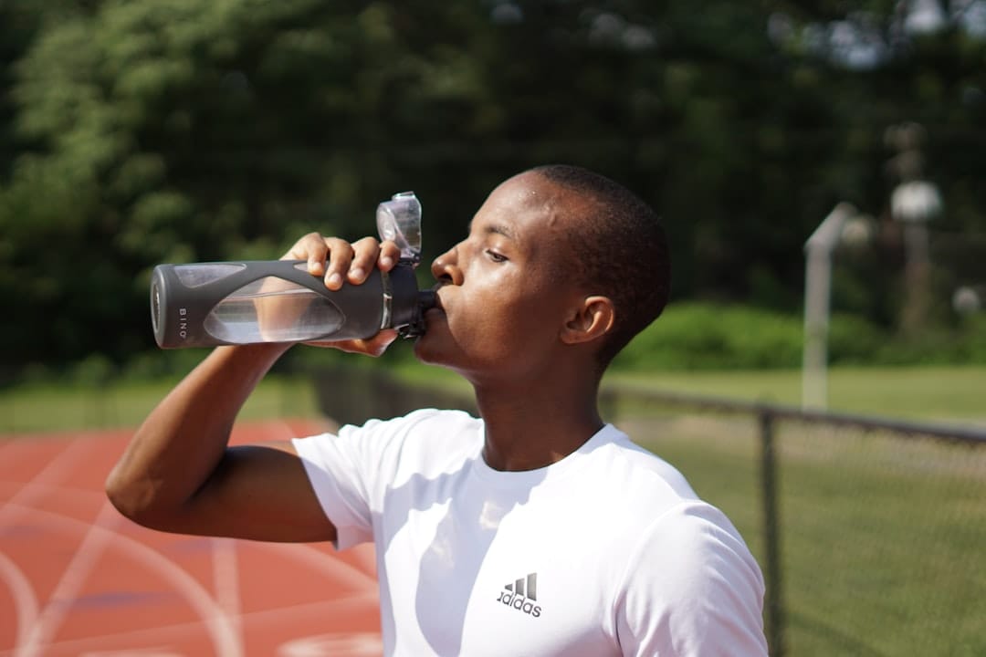 A runner in athletic wear pausing to drink from a water bottle outdoors