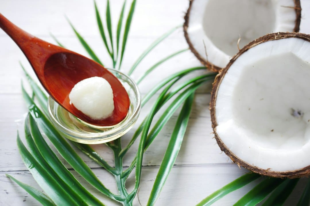 Clear coconut oil in an open glass jar beside a wooden spoon
