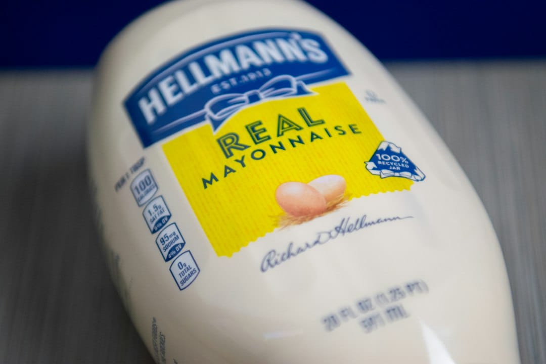An open glass jar of thick white mayonnaise with a spoon resting inside